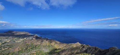 A panoramic view of a coastline with lush hills and a vast blue ocean under a clear sky.