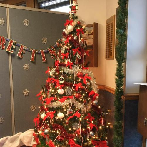 A decorated Christmas tree with red bows, ornaments, and a Santa topper, set in a festive indoor space.