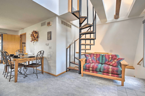 Cozy living space featuring a spiral staircase, colorful couch, and dining area with a table set for four.