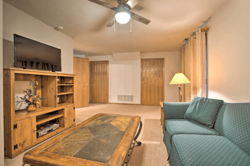 Cozy living room with a green couch, wooden coffee table, TV, and warm lighting from a lamp. Neutral walls and carpet.