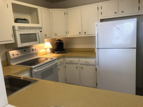 A bright kitchen with white cabinets, a refrigerator, microwave, stove, and a small coffee maker on the counter.