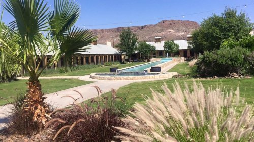 A serene outdoor area featuring a pool, palm trees, and landscaped gardens with mountains in the background.