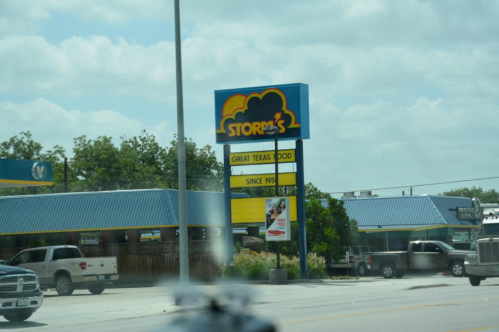Sign for Storm's restaurant featuring "Great Texas Food" and "Since 1985," with a blue roof building in the background.