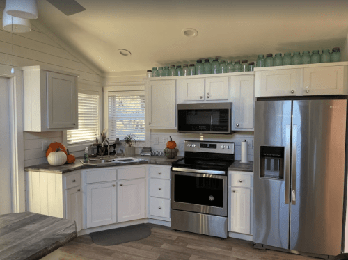Bright kitchen with white cabinets, stainless steel appliances, and decorative pumpkins on the counter.