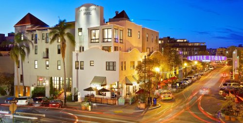 A vibrant hotel at dusk, featuring palm trees and illuminated buildings along a busy street with light trails from cars.