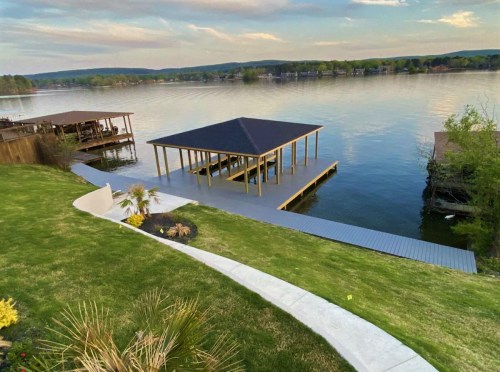 A serene lakeside view featuring a wooden dock and pavilion, surrounded by lush greenery and calm water.