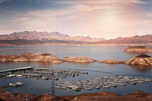 A scenic view of a marina on a lake surrounded by mountains, with a sunset casting a warm glow over the landscape.