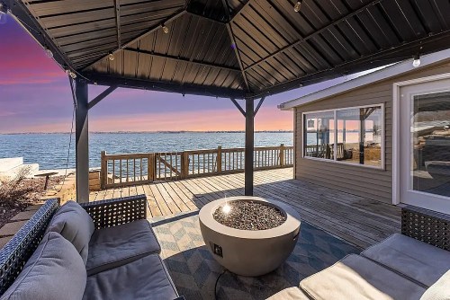 Cozy outdoor seating area with a fire pit, overlooking a serene lake at sunset.