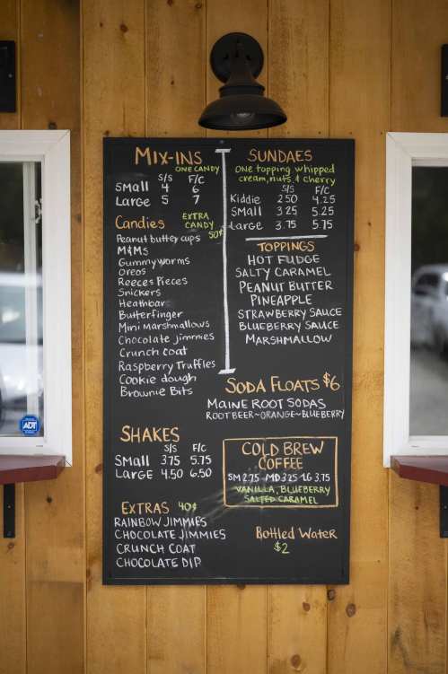 Menu board featuring mix-ins, sundaes, shakes, soda floats, and cold brew coffee options on a wooden background.