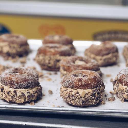 A tray of donuts filled with creamy filling and coated in crushed candy, dusted with sugar.