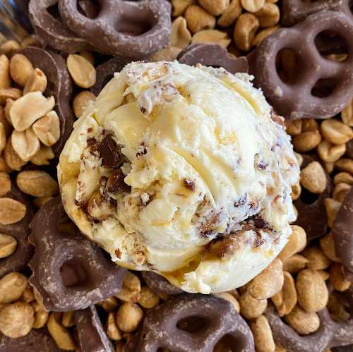A scoop of ice cream surrounded by chocolate-covered pretzels and peanuts.