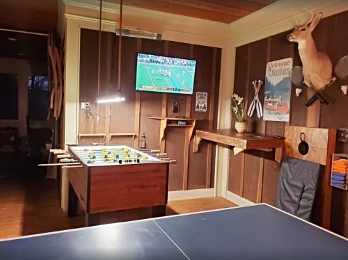 A cozy game room featuring a foosball table, ping pong table, and a TV displaying a sports game on the wall.