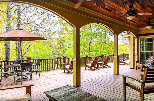 A spacious outdoor deck with seating, an umbrella, and views of lush greenery and trees.