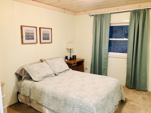 Cozy bedroom with a bed, nightstand, lamp, and curtains, featuring light green walls and framed artwork.