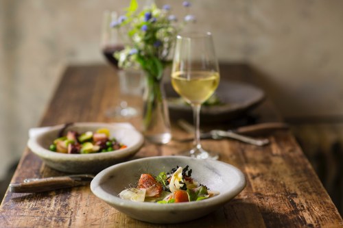 A beautifully arranged table with two dishes, a glass of white wine, and a vase of flowers in a cozy setting.