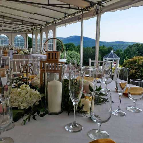 A beautifully set table with glasses and a candle, overlooking a scenic mountain view from a tented venue.