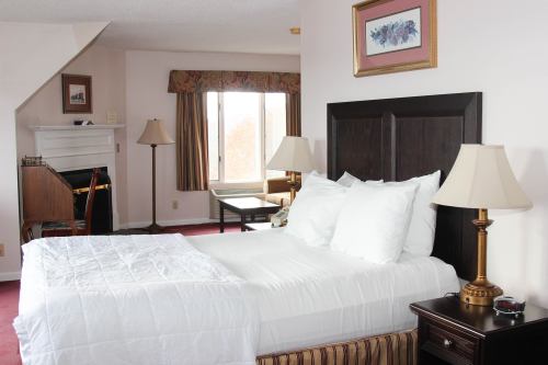 Cozy hotel room with a queen bed, lamps, a desk, and large window with curtains, featuring warm colors and soft lighting.