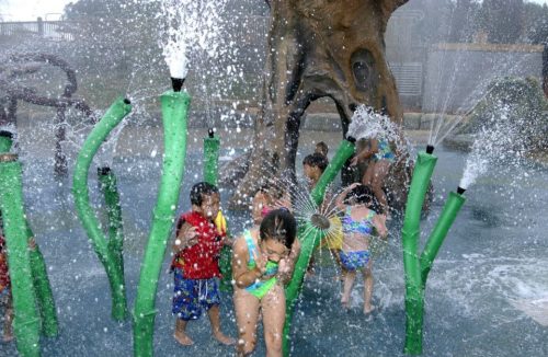 Children play in a splash pad, surrounded by water sprays and colorful structures, enjoying a fun summer day.
