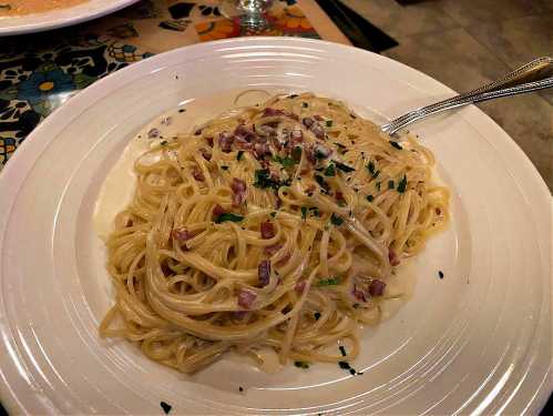 A plate of creamy spaghetti carbonara topped with chopped parsley and bits of pancetta.