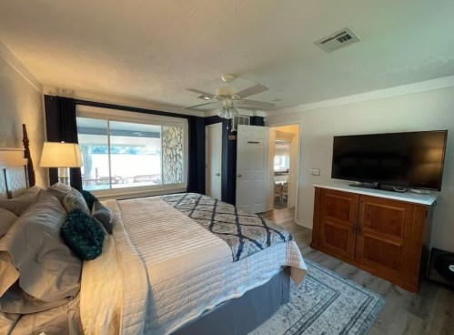 Cozy bedroom with a large window, king-sized bed, TV, and wooden furniture, featuring light colors and a serene atmosphere.