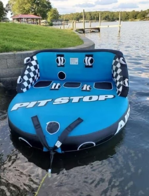 A blue inflatable boat labeled "PIT STOP" floating on calm water near a dock.