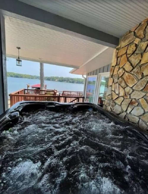 A view from inside a hot tub looking out towards a lake and a deck with seating.