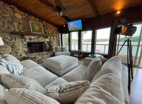 Cozy living room with a stone fireplace, large sectional sofa, and a view of the water through large windows.