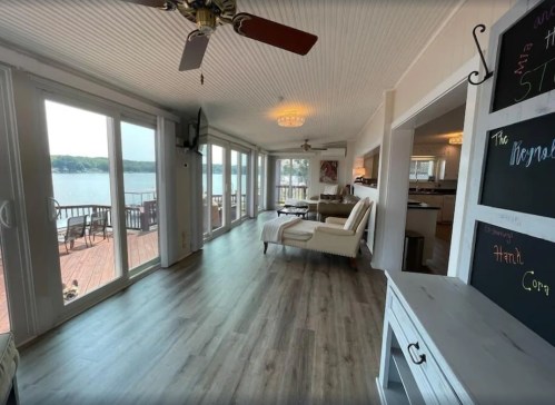 Bright, airy room with large windows overlooking a lake, featuring comfortable seating and a chalkboard wall.