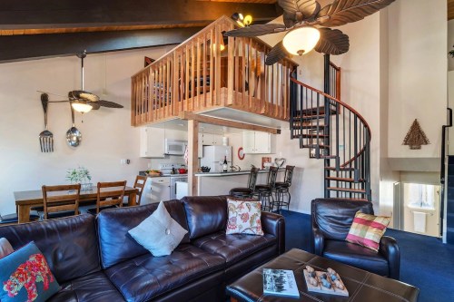 Cozy living area with a spiral staircase, loft, and kitchen, featuring leather sofas and wooden dining furniture.