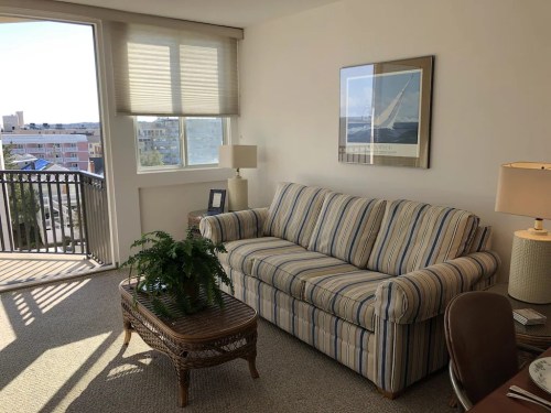 A cozy living room with a striped sofa, a coffee table, a lamp, and a view of the outdoors through a large window.