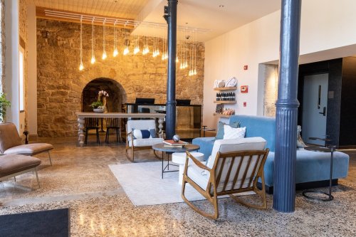 A modern lobby with stone walls, stylish seating, and warm lighting, featuring a reception area and decorative plants.