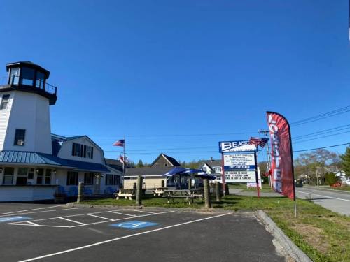 A lighthouse building with a blue roof, flags, and a sign for a lobster restaurant on a clear day.
