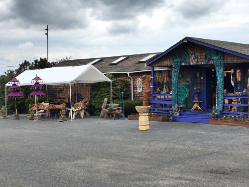 A colorful wooden building with sculptures outside, featuring tents and artistic decor in a cloudy setting.