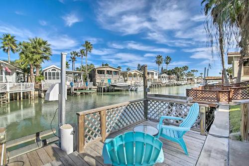 A serene waterfront view with palm trees, colorful houses, and a wooden deck featuring a blue chair and a small table.
