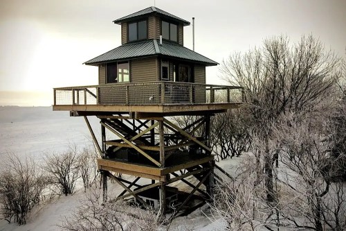 A tall, wooden lookout tower with a metal roof, surrounded by snow-covered trees and a winter landscape.