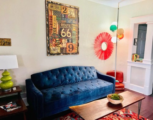 A cozy living room featuring a blue tufted sofa, colorful decor, and a wooden coffee table with a bowl of fruit.