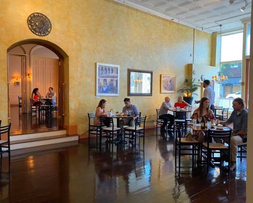 A bright restaurant interior with wooden floors, tables, and diners enjoying meals in a warm, inviting atmosphere.