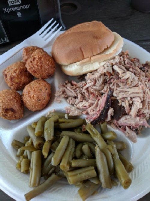 A plate with pulled pork, a bun, green beans, and cornbread balls.