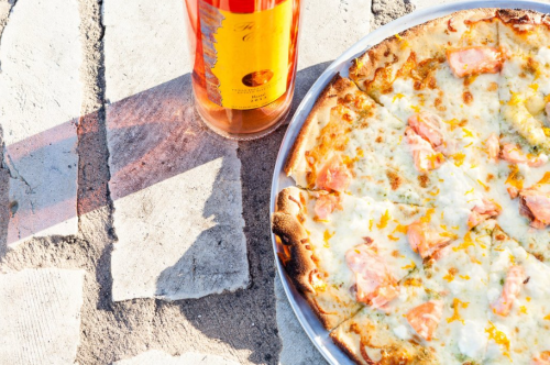 A pizza topped with cheese and salmon sits next to a bottle of rosé wine on a stone surface.