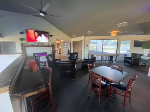 A cozy lounge area with black chairs, a bar, and a large TV, featuring a bright window and modern decor.