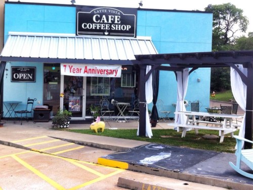 A blue cafe with a sign reading "Latte Vista Cafe," featuring outdoor seating and a banner for a 7-year anniversary.