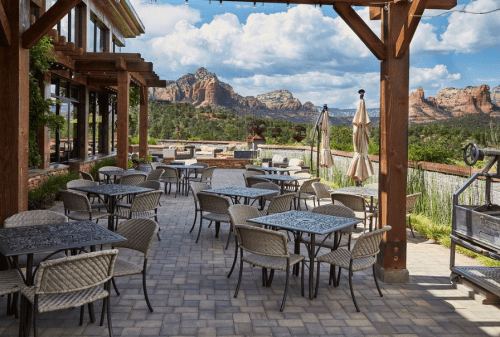 Outdoor dining area with tables and chairs, overlooking scenic mountains under a partly cloudy sky.