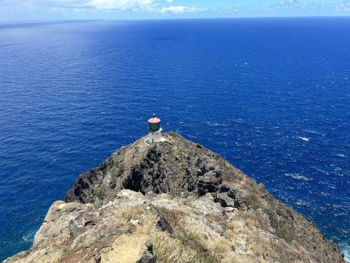 A lighthouse perched on a rocky cliff overlooking a vast blue ocean under a clear sky.