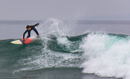 A surfer skillfully rides a wave, performing a maneuver on a bright surfboard against a calm ocean backdrop.