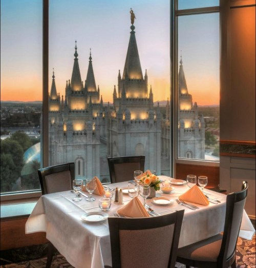 Elegant dining table set for a meal, with a stunning view of a lit-up temple at sunset through large windows.