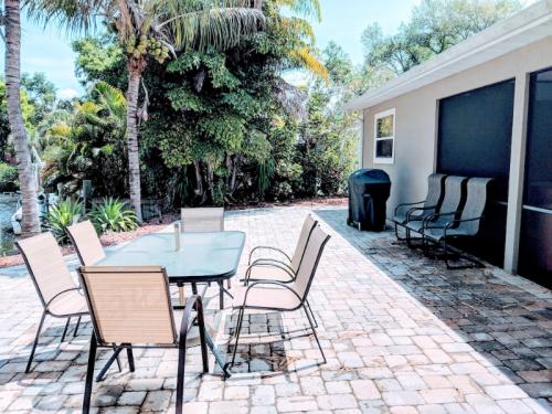 Outdoor patio with a glass table and chairs, surrounded by lush greenery and a grill nearby.