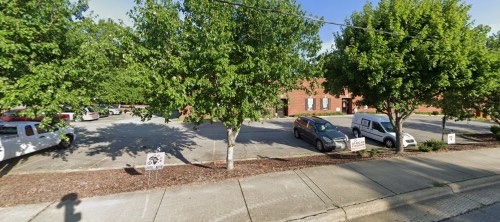 A parking lot with several vehicles and trees lining the sides, next to a brick building.