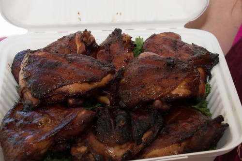 A container filled with grilled, smoky chicken thighs resting on a bed of greens.