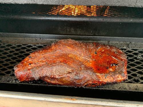 A large, smoked brisket resting on a grill, with a smoky background and a warm glow from the fire.