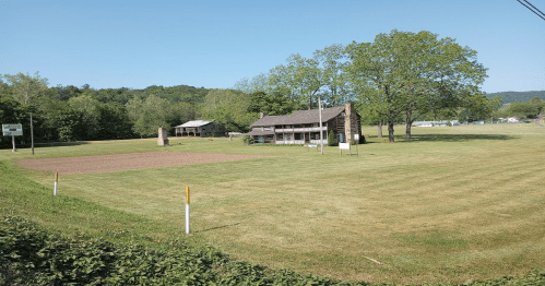 A grassy field with a rustic building and trees in the background under a clear blue sky.